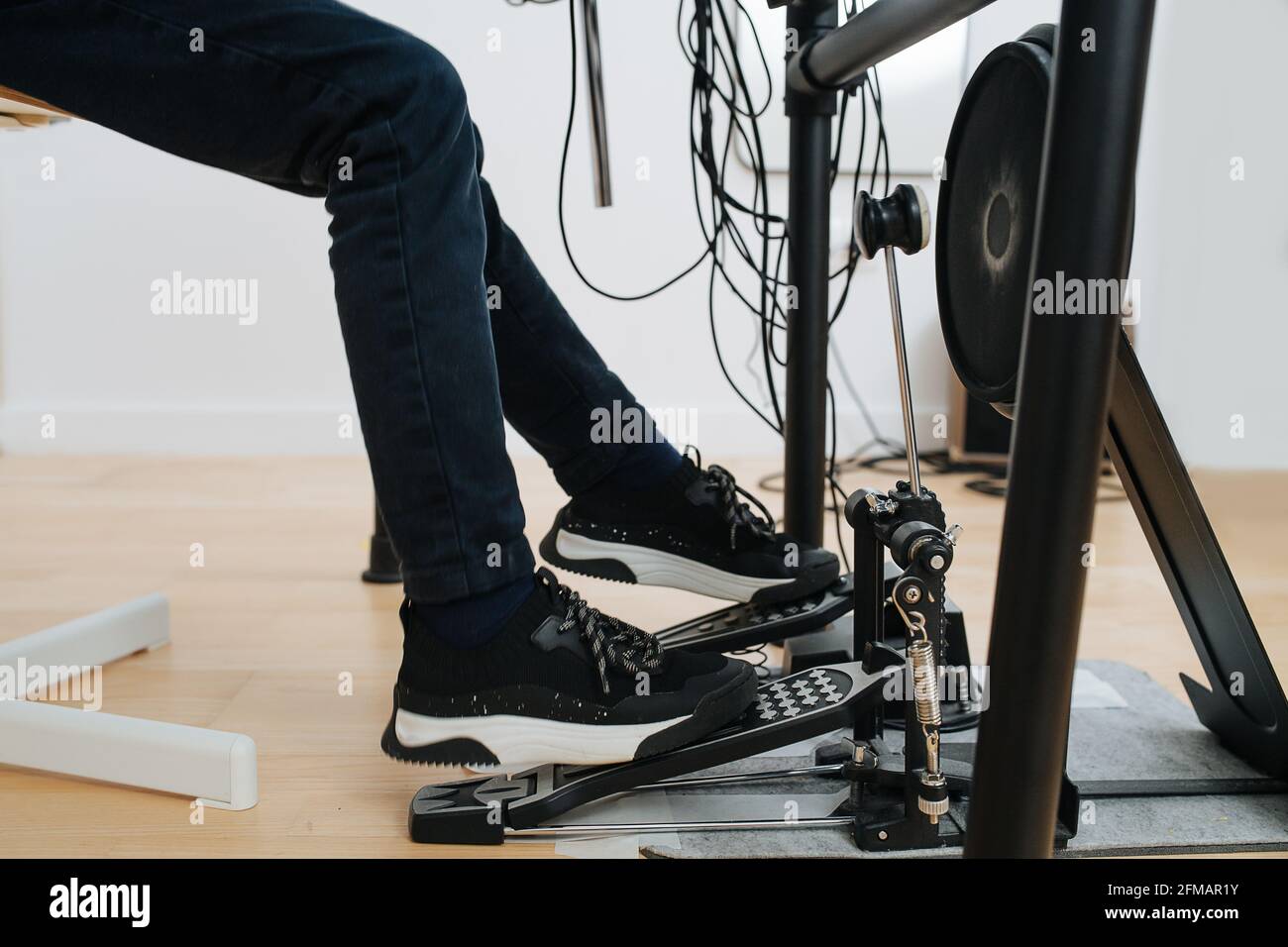 Die Beine eines kleinen Jungen, der elektronische Trommeln spielt und mit Pedalen tritt. Er trägt Jeans und neue stylische Sneaker. Seitenansicht. Stockfoto