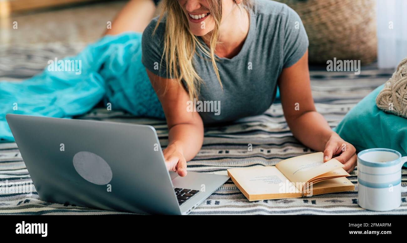 Fröhliche Frau Porträt mit Laptop-Computer zu Hause und Lesen Ein Papierbuch - die Menschen genießen Entspannung und Technologie im Haus - sonntagskonzept und Freizeitaktivitäten im Haus Stockfoto