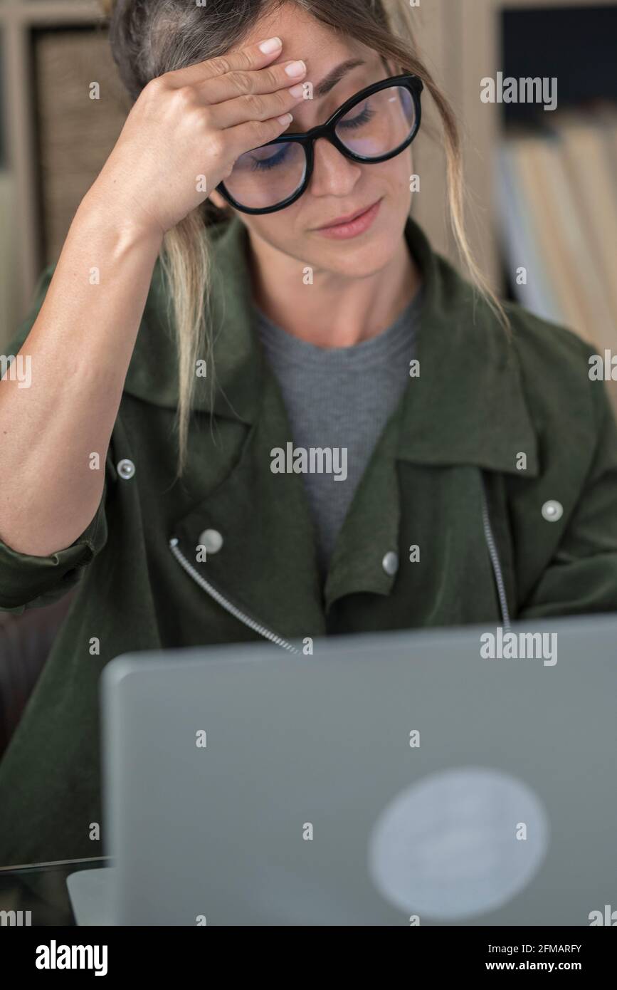 Gestresste tausendjährige kaukasische Frau mit Kopfschmerzen Blick auf Laptop-Bildschirm Arbeit online aus dem Home Office. Müde junge Frau verwenden Computer im Internet auf dem Gerät. Technologiekonzept. Stockfoto