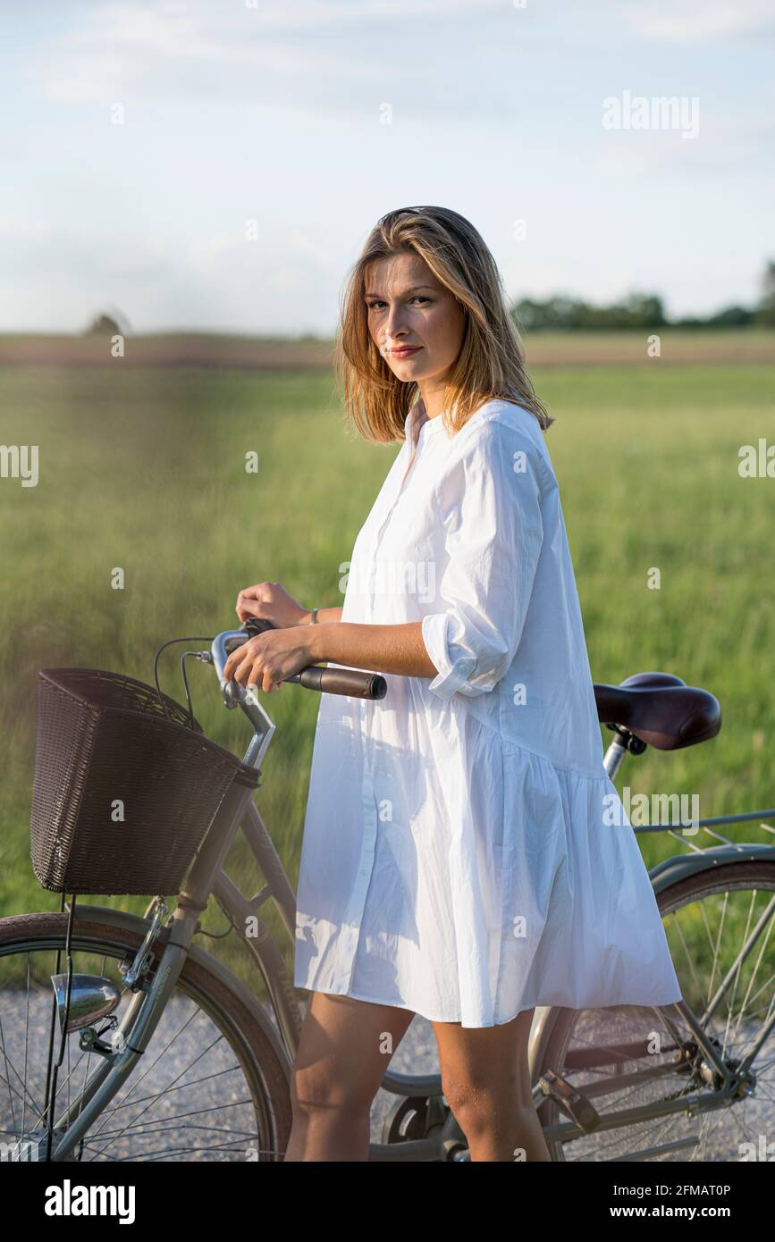 Junge Frau schiebt in der Abendstimmung ein Fahrrad mit Korb, Franken, Bayern, Deutschland Stockfoto