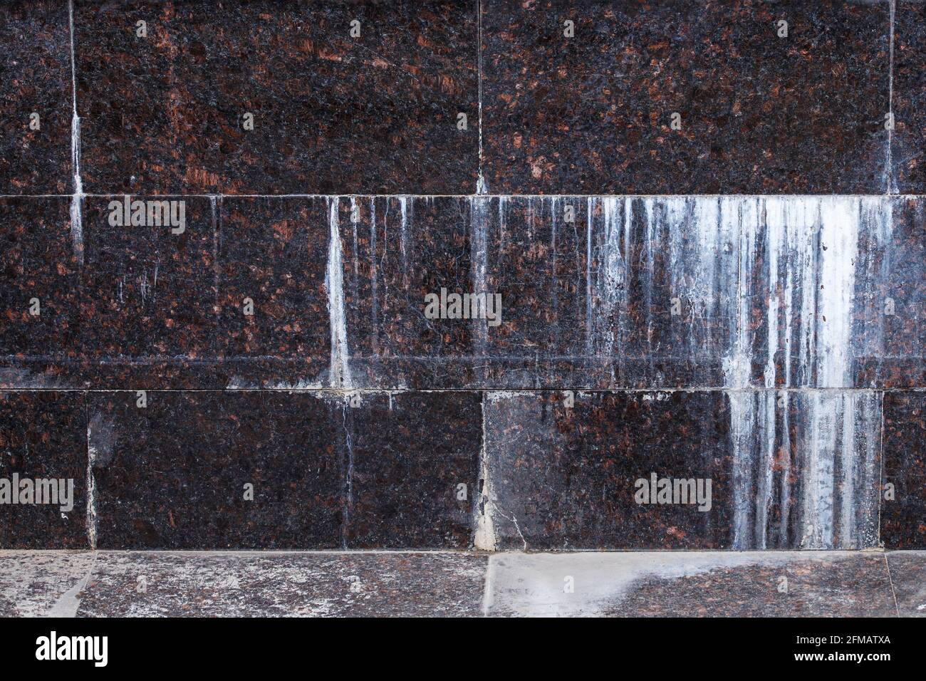 Flache Wand mit rechteckigen Fliesen aus natürlichem braunem Granit mit weißen Mineraltropfen. Stockfoto