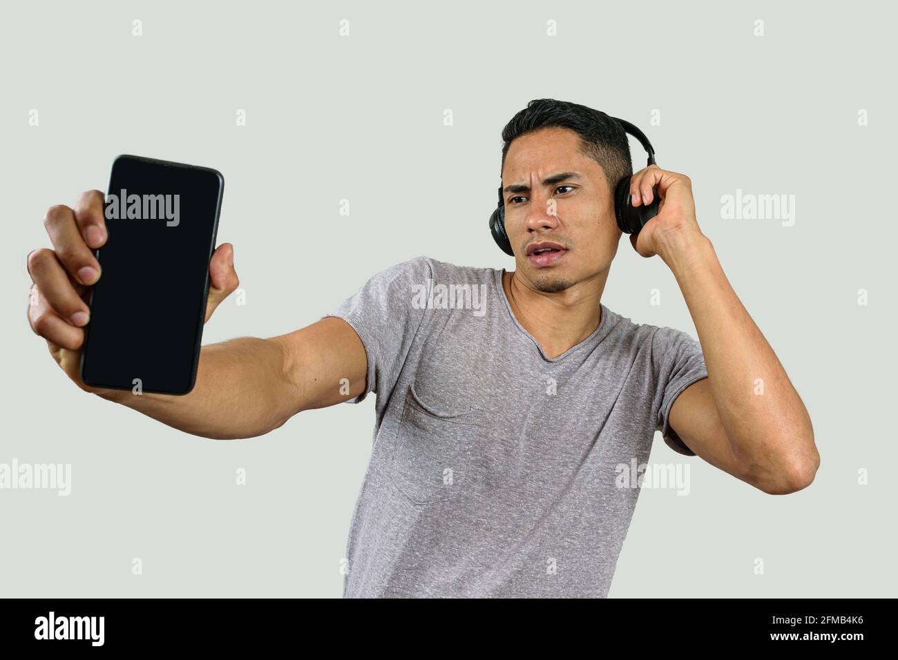 Der 28-jährige Brasilianer mit einer Hand auf dem kabellosen Kopfhörer schaute auf sein Smartphone und zeigte es der Kamera. Stockfoto