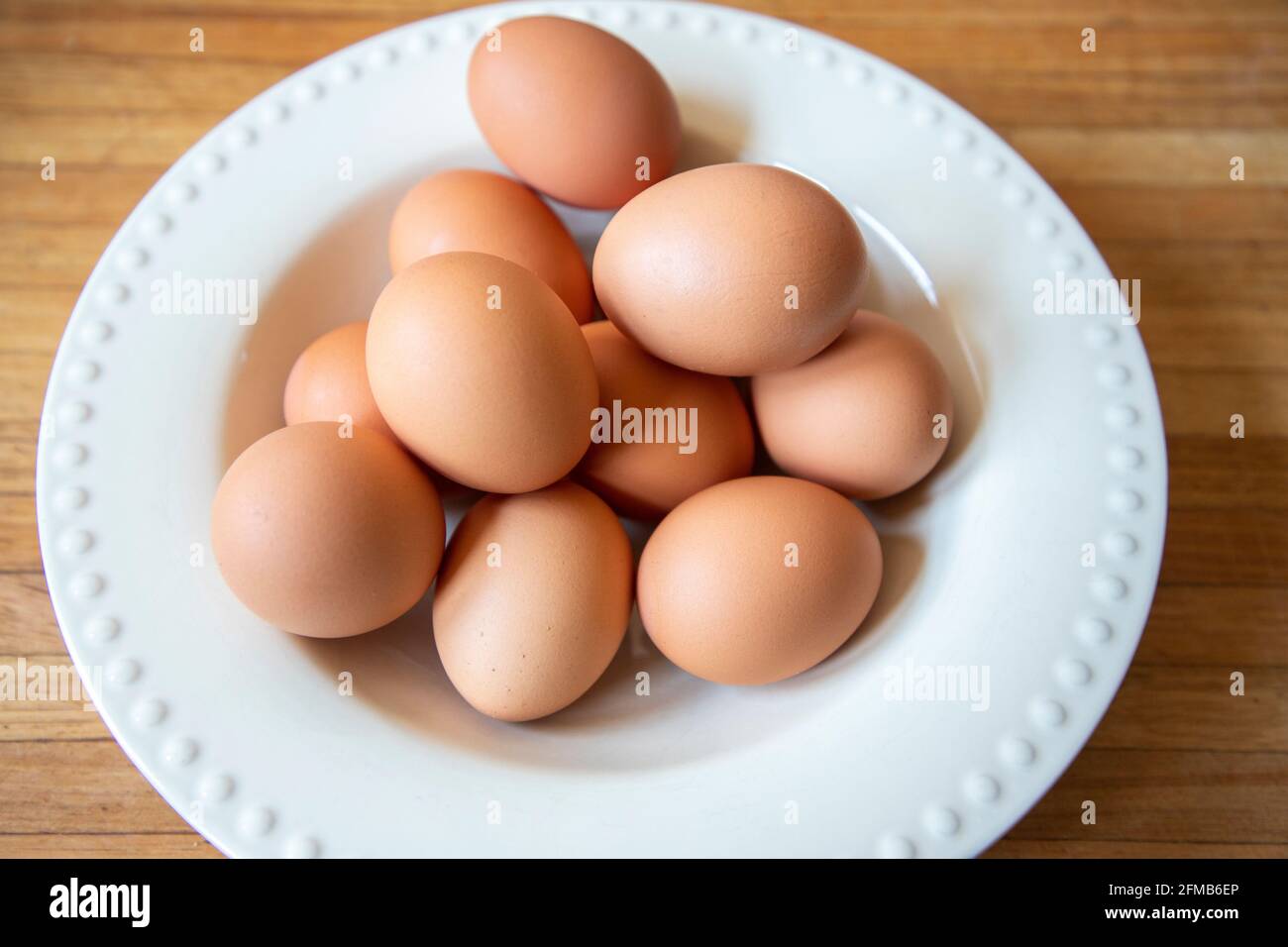 Braune Eier aus biologischem Anbau in einer weißen Schüssel auf einer Holzplatte. Stockfoto