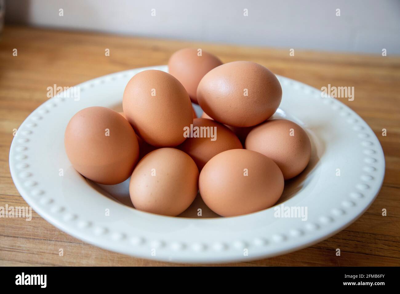 Braune Eier aus biologischem Anbau in einer weißen Schüssel auf einer Holzplatte. Stockfoto