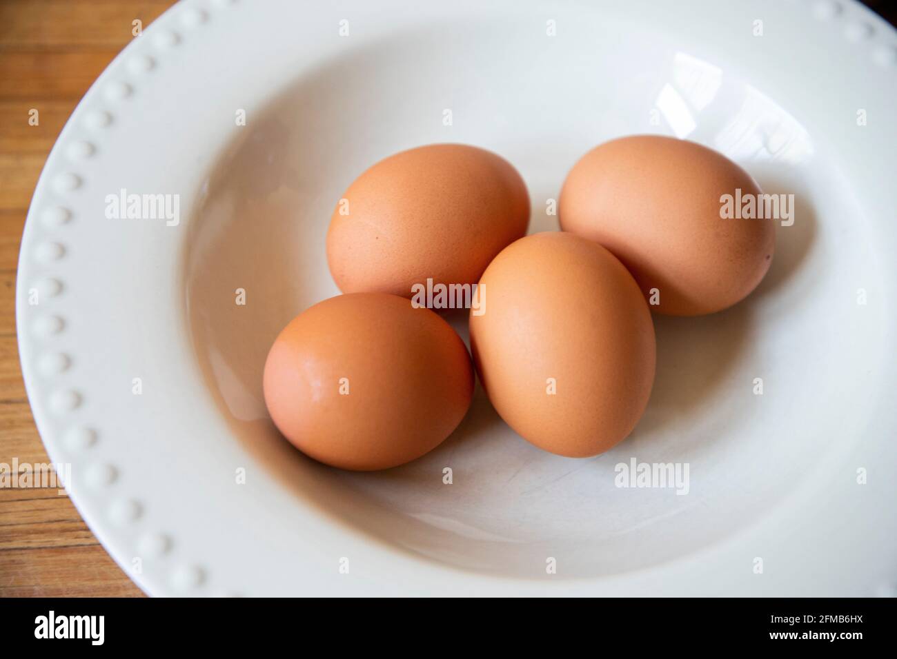 Braune Eier aus biologischem Anbau in einer weißen Schüssel auf einer Holzplatte. Stockfoto
