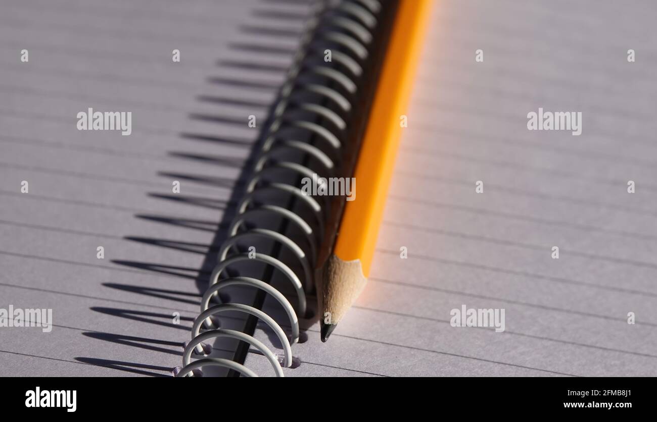 Nahaufnahme eines spitzen Bleistifts auf einem leeren Notizbuch mit Der Schatten der Spiralbindung auf dem Papier Stockfoto