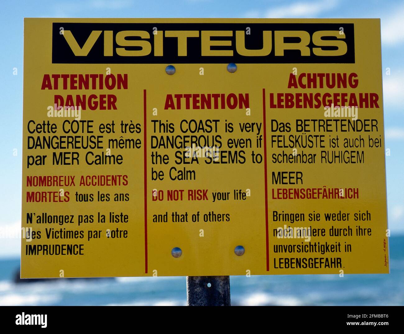Warnschild für Touristen an einer felsigen Küste in drei Sprachen unberechenbarer Gefahren Stockfoto