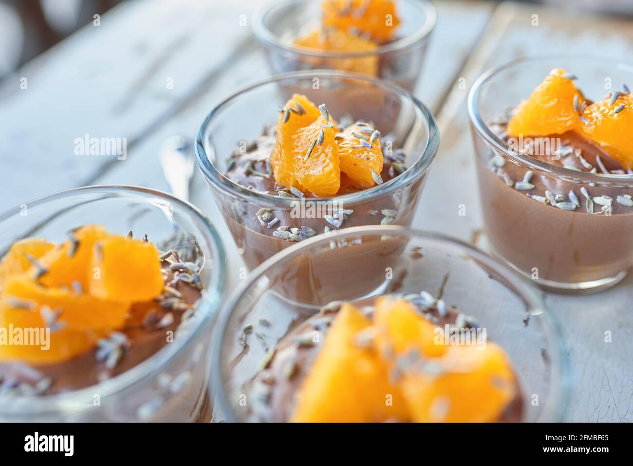 Ayurvedische Küche - Schokoladenmousse mit seidenem Tofu, dekoriert mit Orangenfilets und Lavendelblüten, gefüllte kleine Glasschüsseln stehen auf einem weißen Holztisch Stockfoto