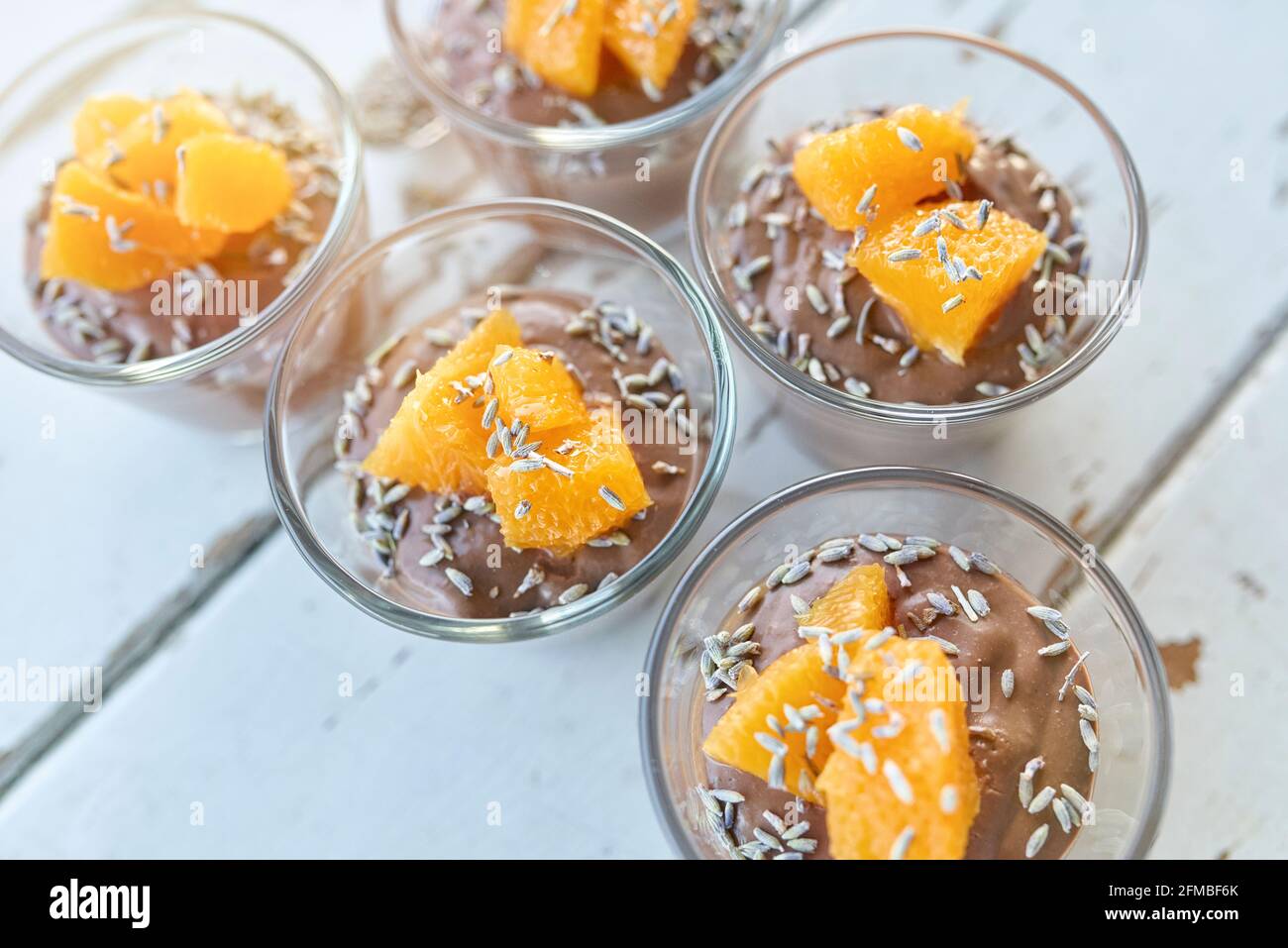 Ayurvedische Küche - Schokoladenmousse mit seidenem Tofu, dekoriert mit Orangenfilets und Lavendelblüten, gefüllte kleine Glasschüsseln stehen auf einem weißen Holztisch Stockfoto