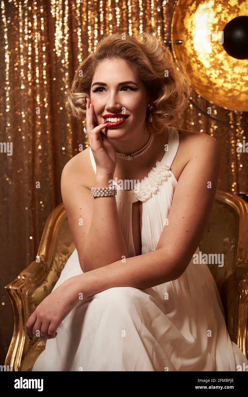 Junge Frau mit blonden Haaren im Marilyn Monroe-Stil in Gold Sessel Stockfoto