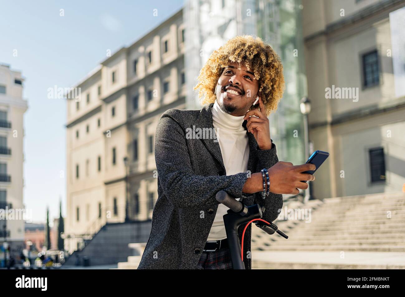 Hübscher intelligenter afrikanischer Mann, der in einem Elektroroller auf der Straße ein Handy tippt. Kommunikationskonzept Stockfoto