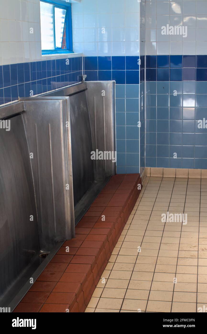 Innen einer männlichen Standup Urinal Toilette aus den 1960er Jahren mit Metall Trog Und Blaue Fliesen Stockfoto