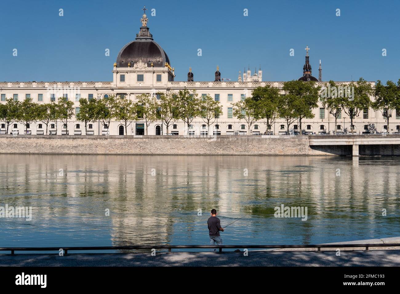Lyon (Frankreich), 03. Mai 2021. Blick auf das Hôtel Dieu und die Fourvière Basilika mit einem Fischer im Vordergrund am Ufer der Rhone. Stockfoto