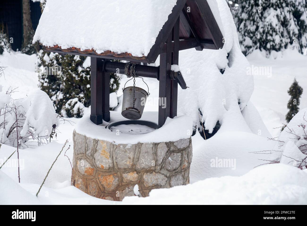 Verschneite Wasserbrunnen mit Metalleimer in einem Garten. Stockfoto