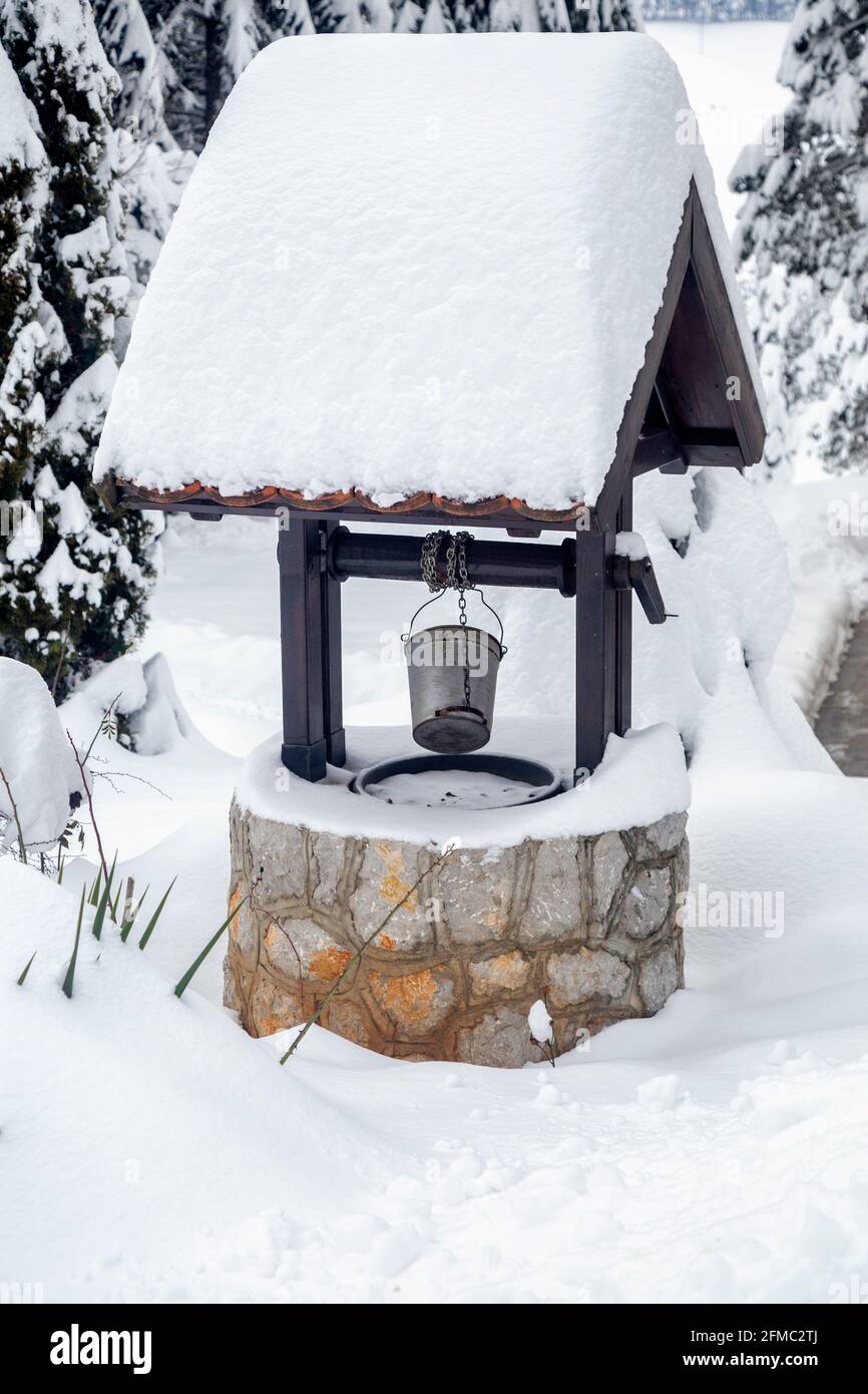 Schnee bedeckt gut mit Metalleimer in einem Garten. Stockfoto