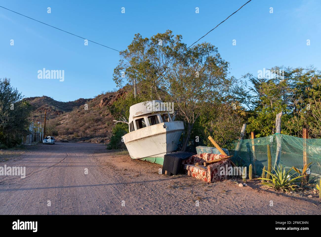 Ein Fiberglas-Fischerboot, eine Couch und andere Haushaltsgegenstände, die auf einer Schotterstraße in der Wüste von Mexiko ordentlich zur Müllabfuhr gestapelt wurden. Stockfoto