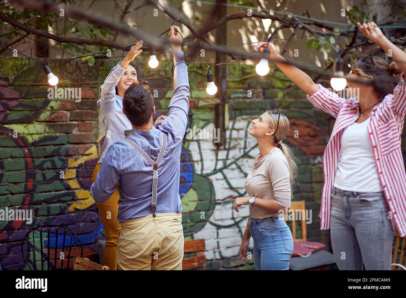 Eine Gruppe fröhlicher Freunde bereitet den Garten einer Bar für eine Party an einem schönen Tag vor. Freizeit, Bar, Freundschaft, Outdoor Stockfoto