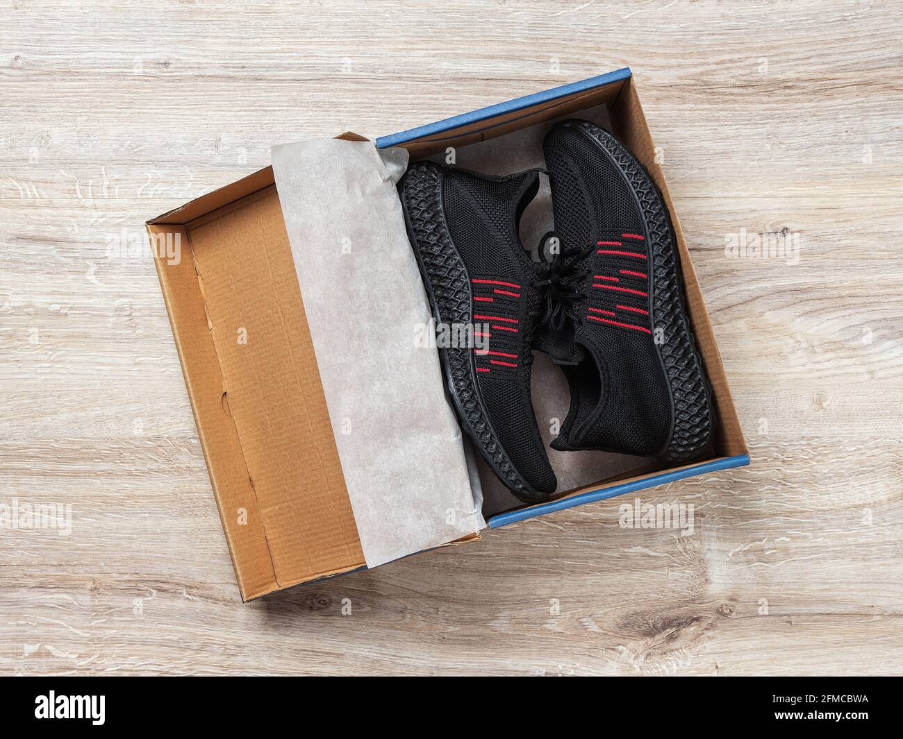 Ein Paar schwarze Mesh-Sneakers in einer braunen Pappschachtel auf dem Boden. Moderne atmungsaktive Schuhe für heißen Sommer. Offene Box mit neuen Herrenschuhen für ein aktives Leben Stockfoto