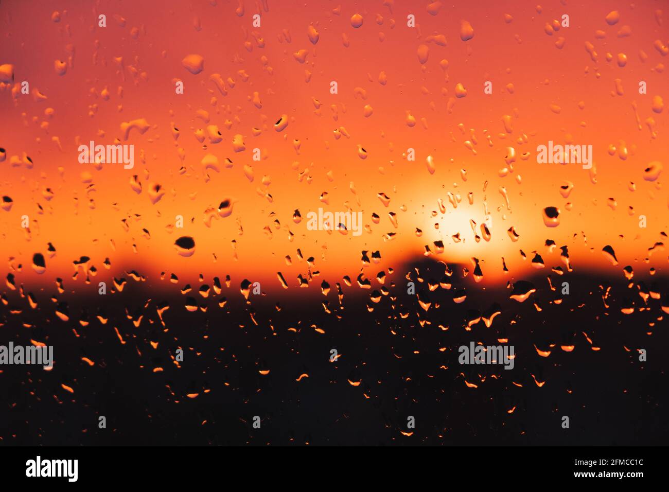 Regentropfen auf dem Fenster gegen den Abendhimmel. Regentropfen auf dem Glas, Sonnenuntergang, wetterbezogenes Bild Stockfoto