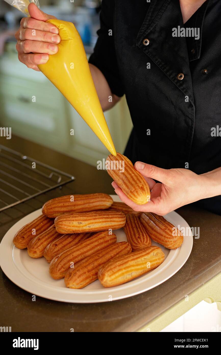 Französisches Dessert eclair. Der Konditor füllt die Ecolirs mit Creme. Gebäck Pudding Kuchen mit Creme. Weicher, selektiver Fokus. Stockfoto