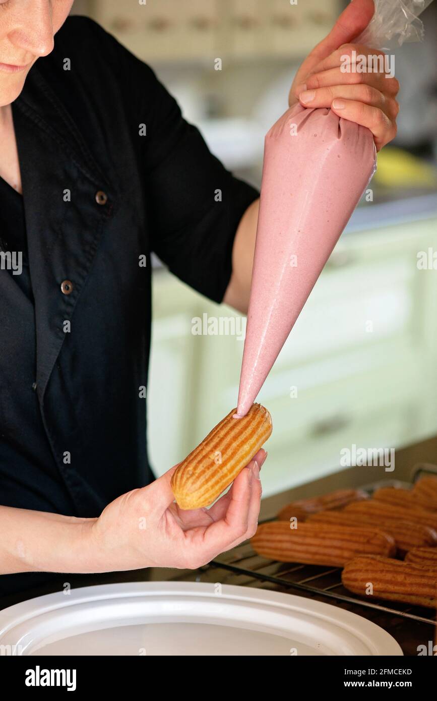 Französisches Dessert eclair. Der Konditor füllt die Ecolirs mit Creme. Gebäck Pudding Kuchen mit Creme. Weicher, selektiver Fokus. Stockfoto