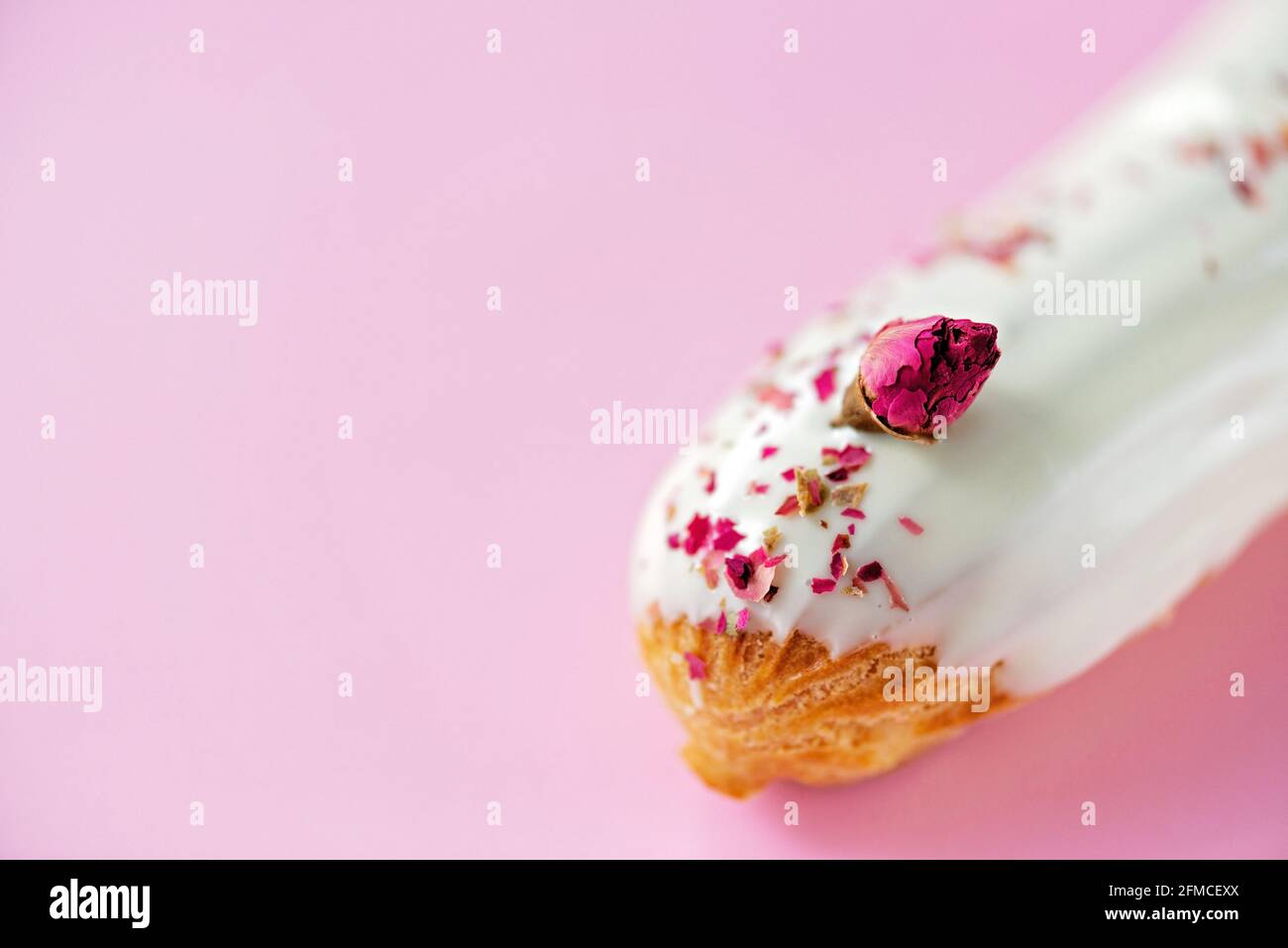 Französische Dessert-Eclare oder Profiteroles mit weißer Schokoladenglasur mit Rosengeschmack auf einem rosa Hintergrund. Kuchen mit Pudding, Rosencreme und toppi Stockfoto