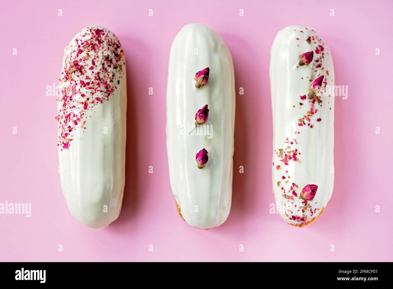 Französische Dessert-Eclare oder Profiteroles mit weißer Schokoladenglasur mit Rosengeschmack auf einem rosa Hintergrund. Kuchen mit Pudding, Rosencreme und toppi Stockfoto