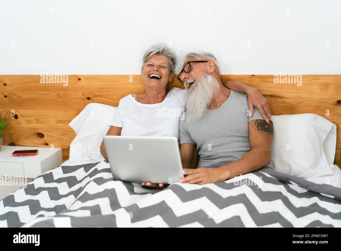 Glückliches Seniorenpaar, das Spaß hat, Medien auf dem Computer im Inneren zu sehen Bett - Ältere Menschen lieben und Beziehungskonzept Stockfoto