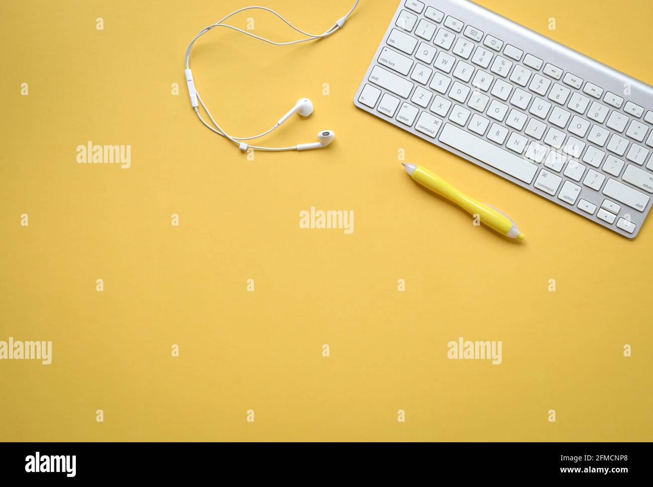 Gelber Schreibtisch mit Computertastatur, Ohrhörer und gelbem Stift. Speicherplatz kopieren. Stockfoto