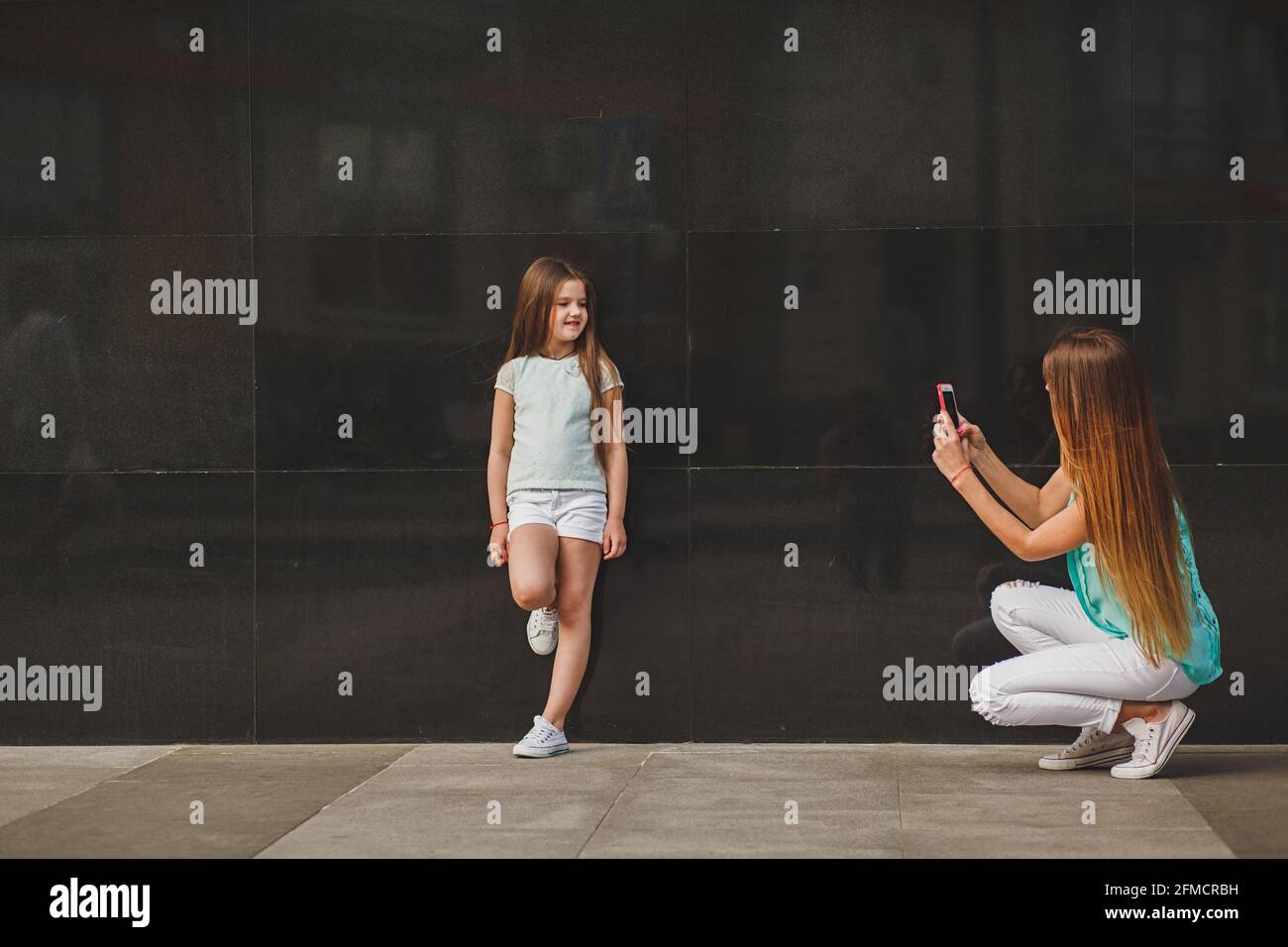 Glückliche Mutter, portrait Kind auf dem Smartphone in der Stadt, der Familie das Tragen eines T-Shirts und Weiße Shorts Stockfoto