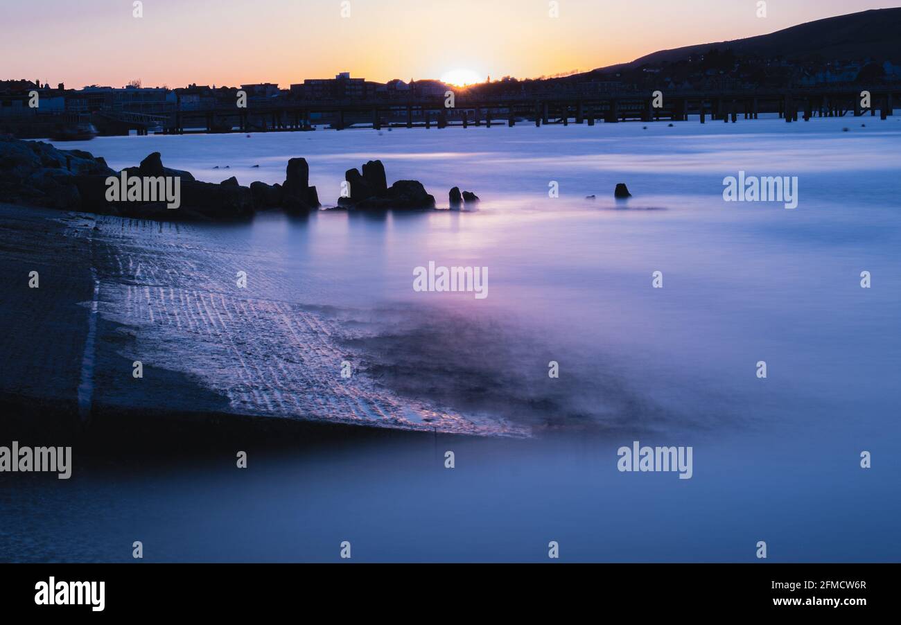 Sonnenuntergang über der Swanage Bay und der kopfsteingepflasterten Bootsrampe Dorset Stockfoto