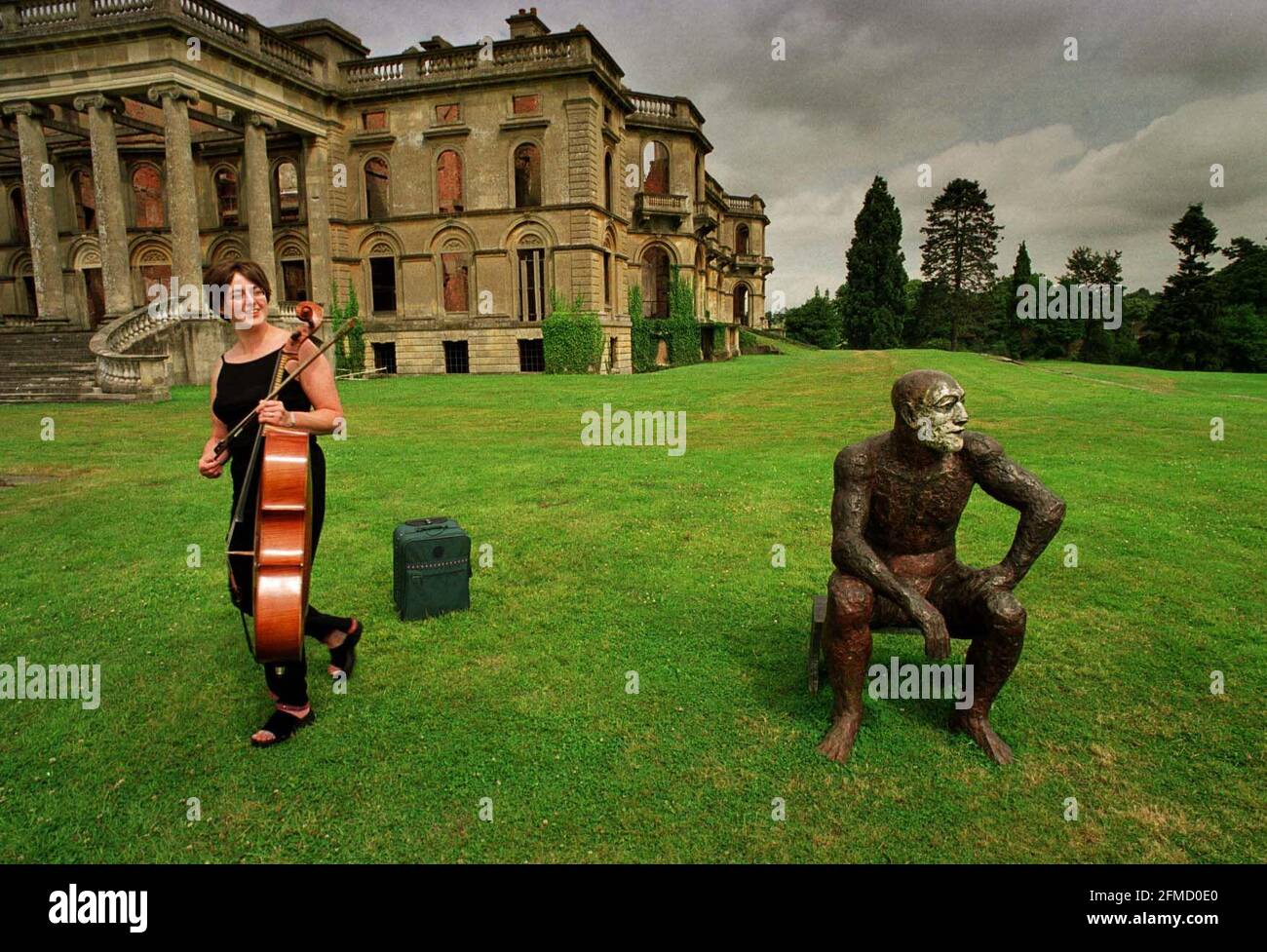 Sitzende Mann-Skulptur von Elizabeth Frink am Witley Court Juli 2000Mitglied des Bellini Streichquartetts spielt neben sitzend Mann von Elizabeth Frink Stockfoto