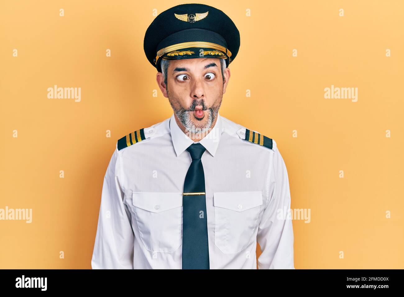 Schöner Mann mittleren Alters mit grauen Haaren trägt Flugzeug Pilot Uniform machen Fisch Gesicht mit Lippen, verrückt und komisch Geste. Lustiger Ausdruck. Stockfoto