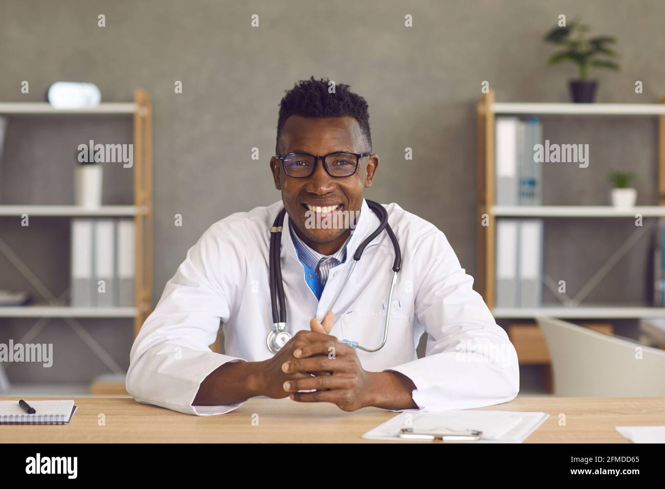 Der männliche Arzt sitzt vor einer Webcam und führt eine Online-Konsultation mit einem Patienten durch. Stockfoto