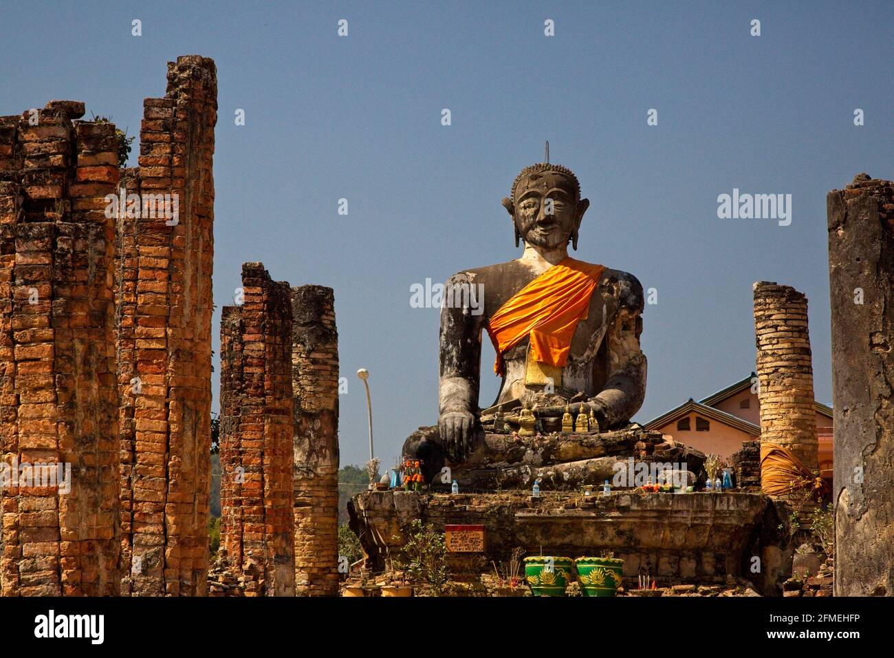 Riesige Steinstatut von buddha, der nach vorne blickt, eingewickelt in orangener Uhrenmonasterie Phonsavan, Laos. Stockfoto