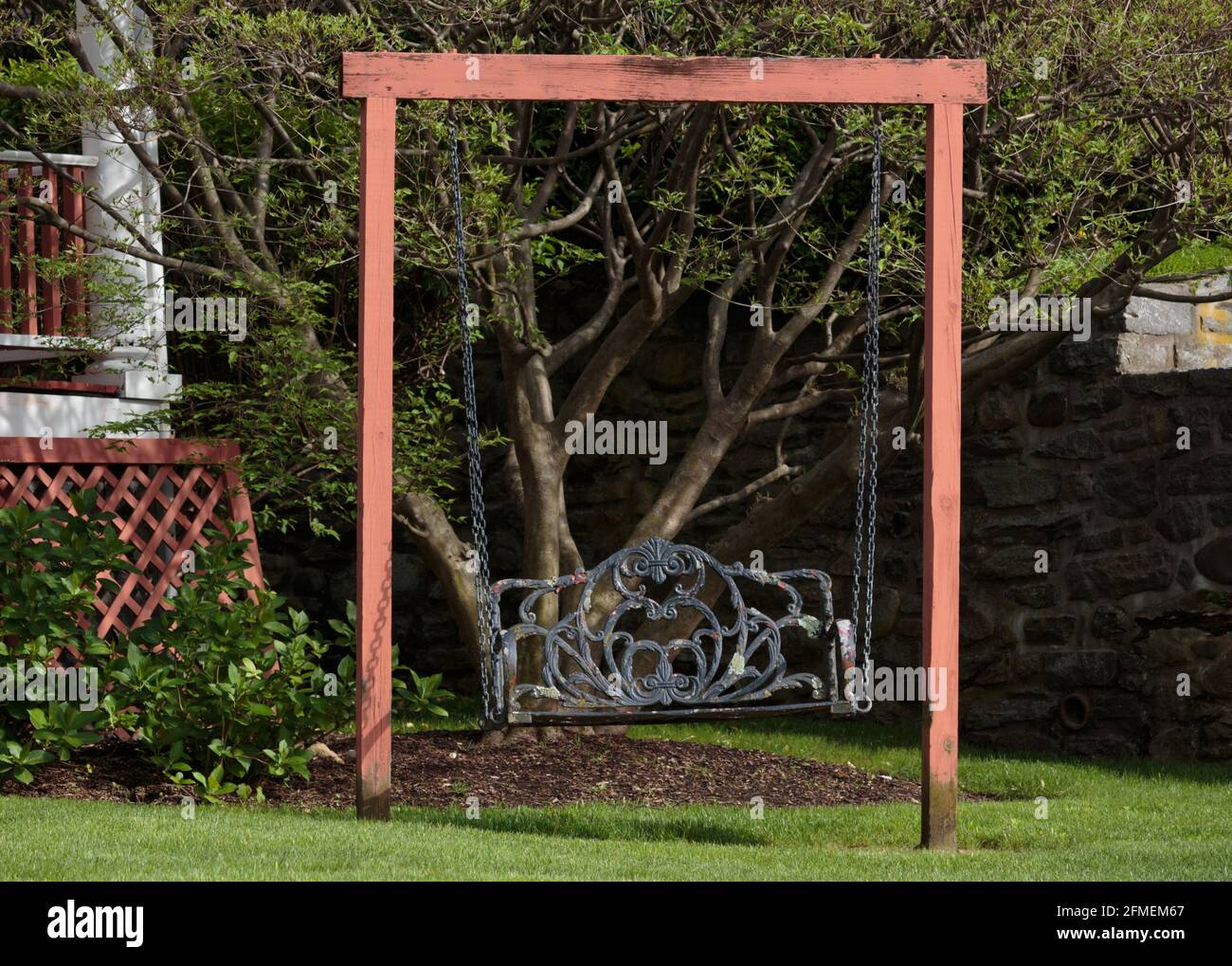 Ein verzierter, verzweifelter, schmiedeeiserner Garten, der in einem malerischen Vorgarten mit einem grünen Rasen, idealistisch und malerisch, schaukelt Stockfoto