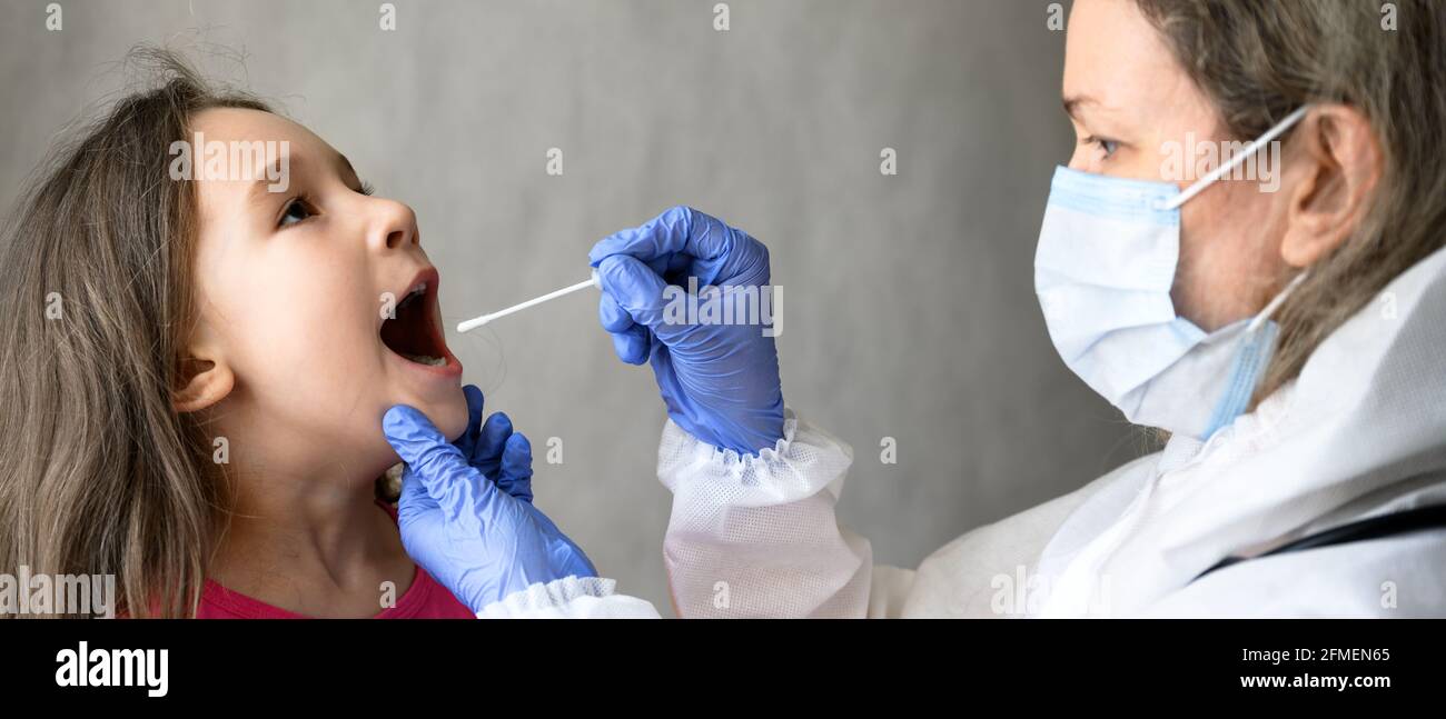 Kid öffnet den Mund für den COVID-19 PCR-Test, der Arzt hält während der Corona-Virus-Pandemie einen Abstrich für die Speichelprobe eines kleinen Mädchens. Panoramablick auf Krankenschwester und Stockfoto