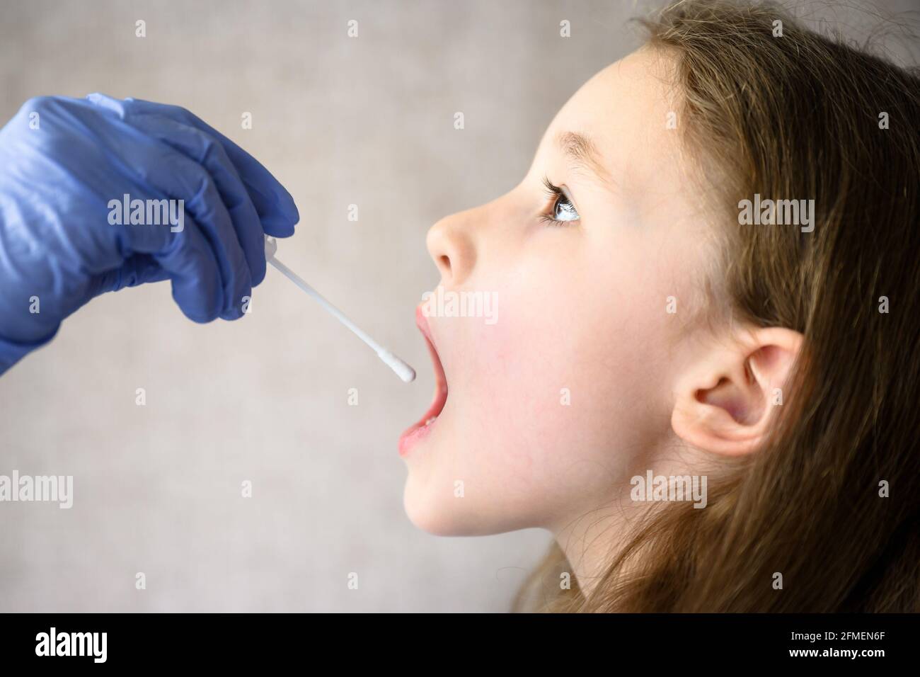 Das Kind öffnet den Mund für den COVID-19 PCR-Test, der Arzt hält während der Coronavirus-Pandemie den Tupfer für die Speichelprobe des niedlichen Kindes. Krankenschwester Hand und kleines Mädchen fac Stockfoto