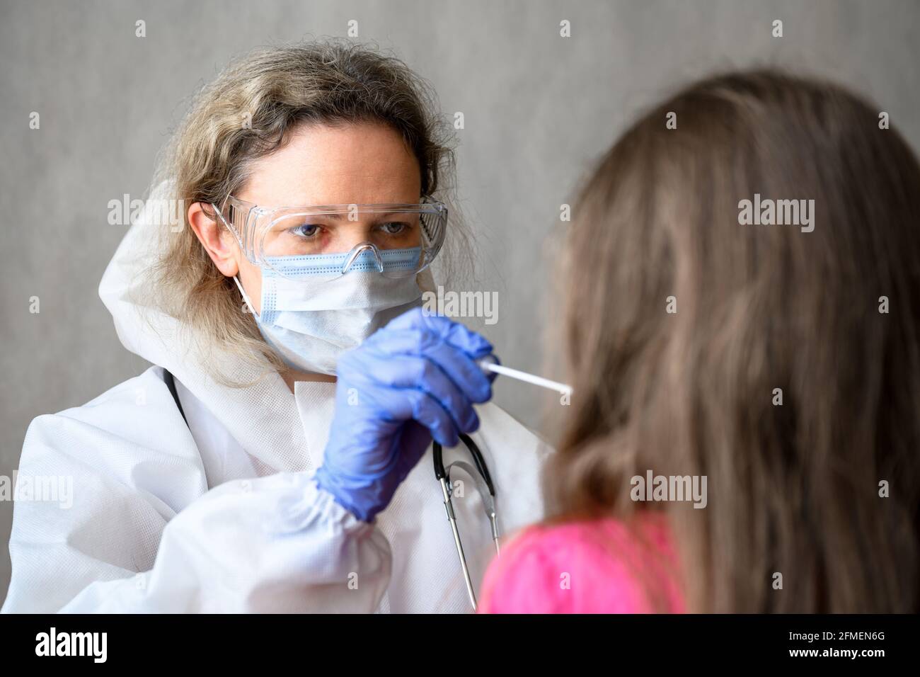 COVID-19-Test in der Klinik hält der Arzt einen Tupfer für Schleimproben aus der Nase oder dem Mund des Kindes. Porträt des Kinderarztes, der während des Corona-Virus mit dem Kind arbeitet Stockfoto