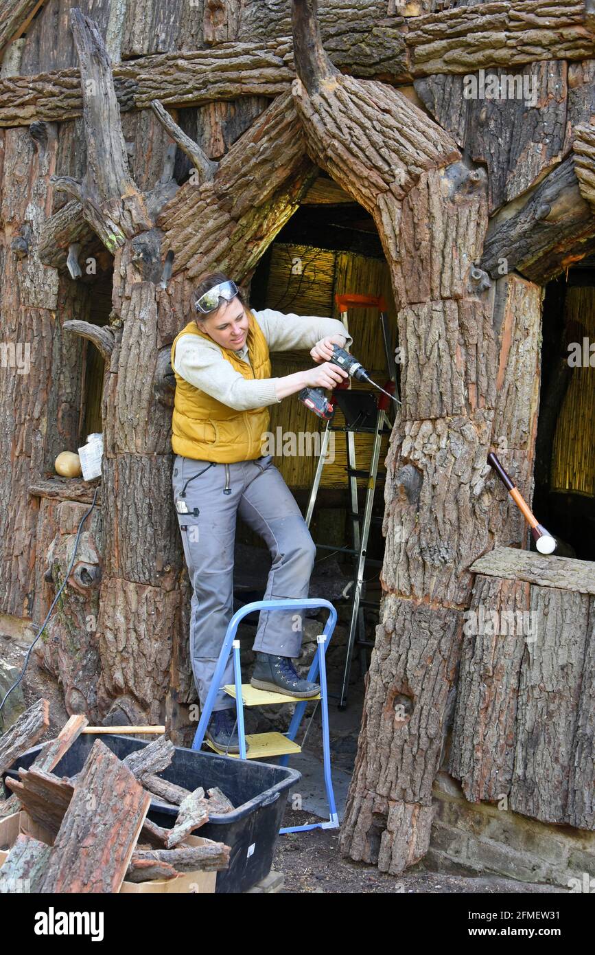 08. Mai 2021, Sachsen-Anhalt, Wörlitz: Die Diplom-Restauratorin Kerstin Klein bringt die letzten Teile der Plattenplatten an den fehlenden Teilen des über 230 Jahre alten Borkenhäusern im Wörlitzer Park an. Das kleine Holzhaus, auch Wurzelhütte genannt, wurde in den letzten zwei Jahren umfassend restauriert. Die Borkenhäuser dienten Prinz Franz als privates Badehaus zum Umkleiden vor dem Schwimmen im Wörlitzer See und sind außen mit knarrierten Eichenstämmen, Platten und Rinde verkleidet. Innen schmücken Kassen aus Ulmenhalbstämmen und mit handgewebten Schilfmatten und Rush-Zöpfen die Wände und die Decke. Der Park wurde angelegt Stockfoto