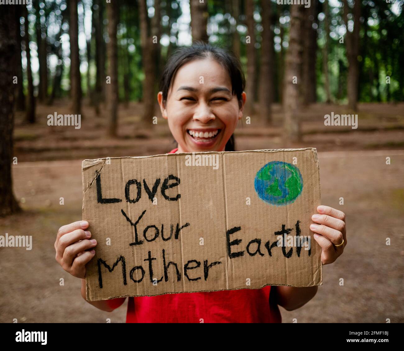 Die junge Frau mit Transparenten, die gegen Umweltverschmutzung und globale Erwärmung im Wald protestieren, um den Planeten Erde zu retten. Das Konzept des Weltumwelttages. Stockfoto