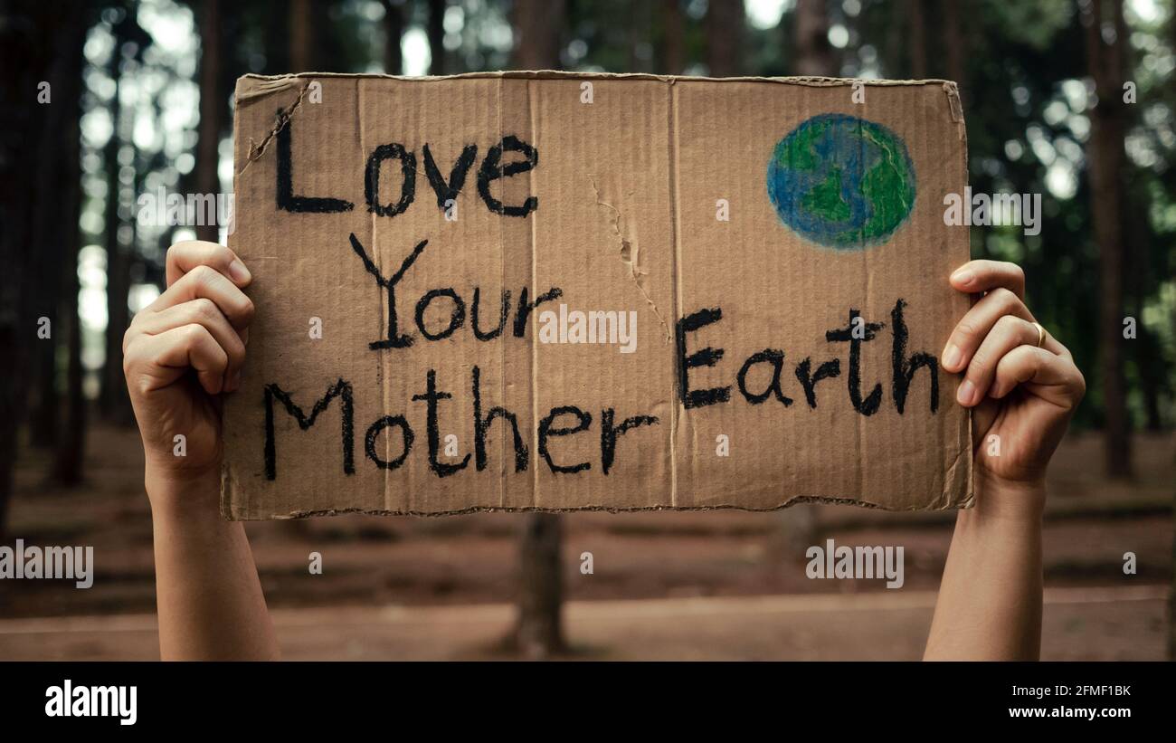 Hand hält Banner, die gegen Verschmutzung und globale Erwärmung im Wald protestieren, um den Planeten Erde zu retten. Das Konzept des Weltumwelttages. Stockfoto