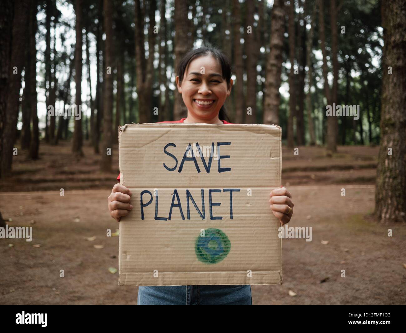 Die junge Frau mit Transparenten, die gegen Umweltverschmutzung und globale Erwärmung im Wald protestieren, um den Planeten Erde zu retten. Das Konzept des Weltumwelttages. Stockfoto