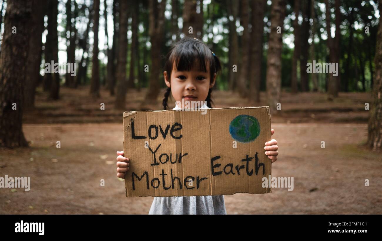 Das kleine Mädchen mit Transparenten, die gegen Umweltverschmutzung und globale Erwärmung im Wald protestieren, um den Planeten Erde zu retten. Das Konzept der Weltumwelt D Stockfoto
