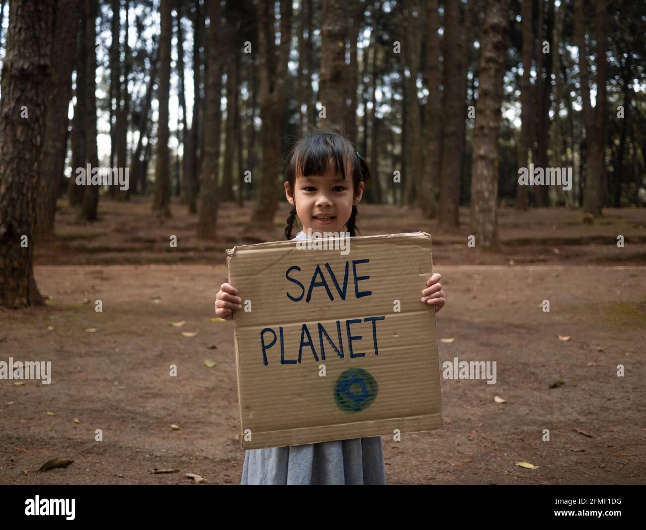 Das kleine Mädchen mit Transparenten, die gegen Umweltverschmutzung und globale Erwärmung im Wald protestieren, um den Planeten Erde zu retten. Das Konzept der Weltumwelt D Stockfoto