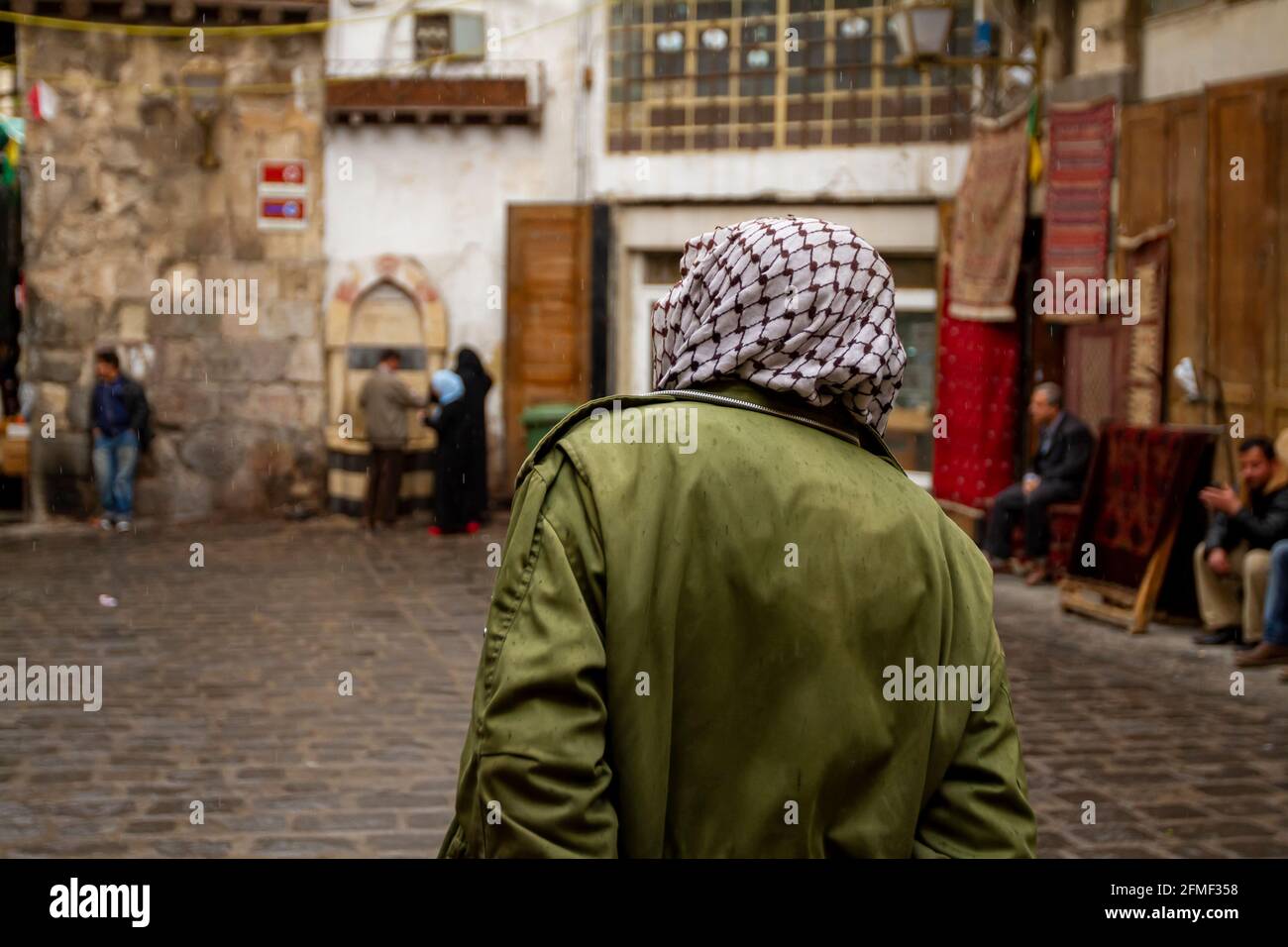 Blick auf die Straße, Innenstadt von Damaskus, Syrien, mit einem Mann von hinten, der in der Altstadt von Damaskus, Syrien, einen Keffiyeh im palästinensischen Stil trägt. Kopfsteinpflaster Stockfoto
