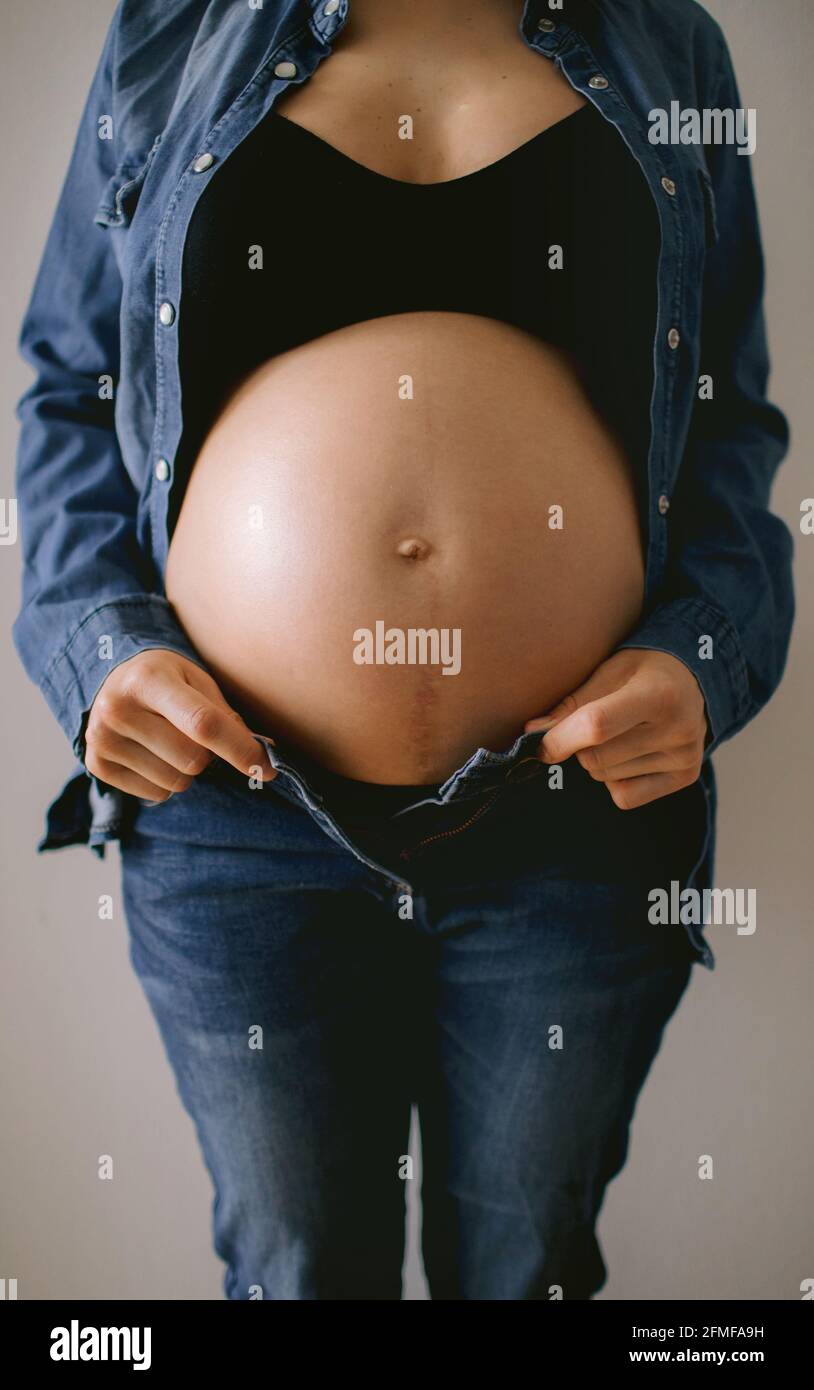 Eine Schwangerin berührt ihren Bauch in der Nähe der Fenster. Schwangerschaft und Mutterschaft Konzept. Stockfoto