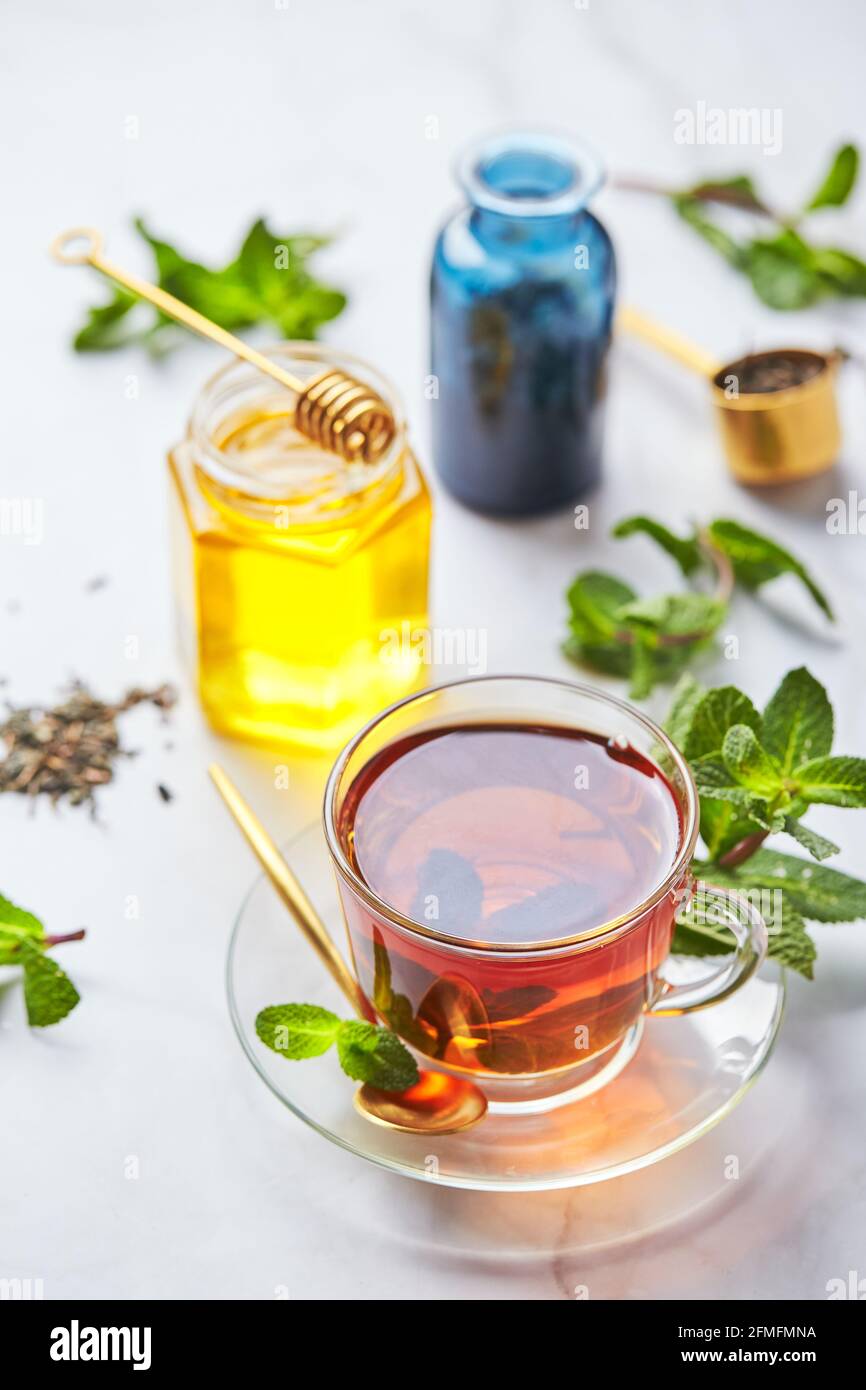 Schwarzer Tee in Glas durchsichtiger Becher mit Minzblättern und Honig. Beruhigender und revitalisierender Tee, Anti-Stress und Entspannung. Stockfoto