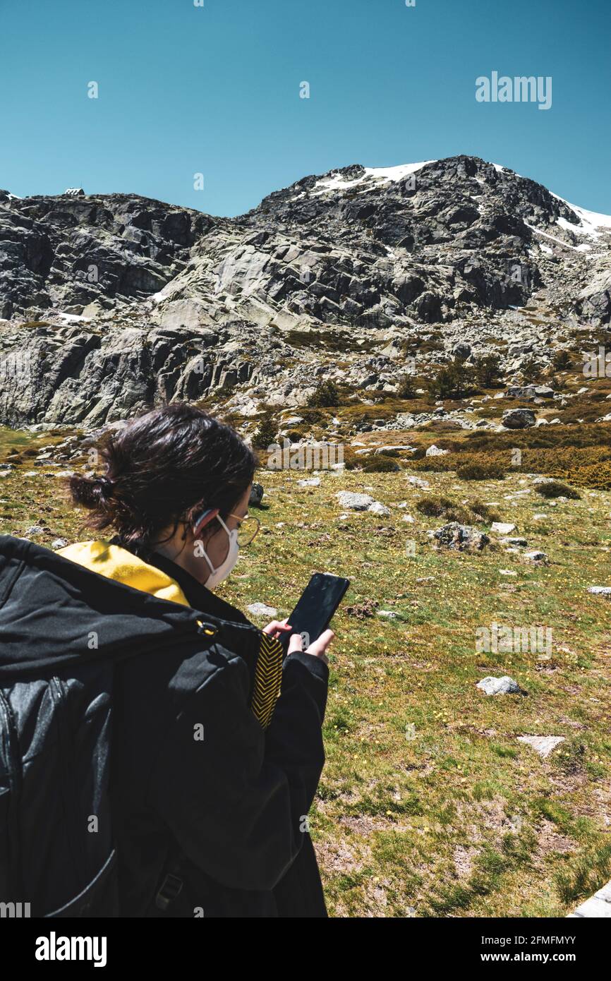 Das junge Mädchen trägt eine Maske auf dem Berg, während es ihr Smartphone benutzt, um zu finden, wo sie sich befindet. Stockfoto