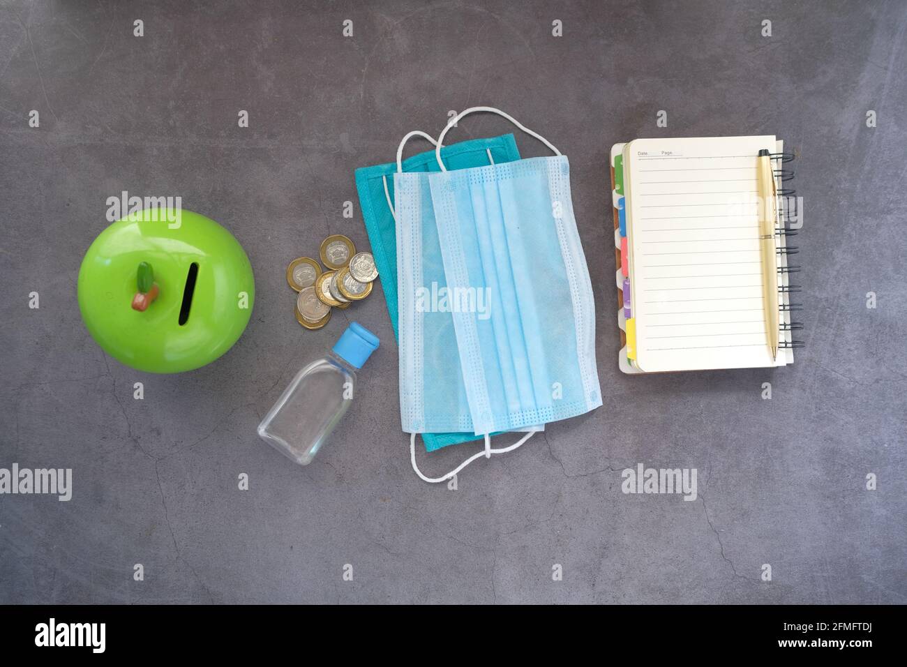 Münzen sparen in einem Glas mit Gesichtsmaske und Hand Desinfektionsmittel auf dem Tisch Stockfoto